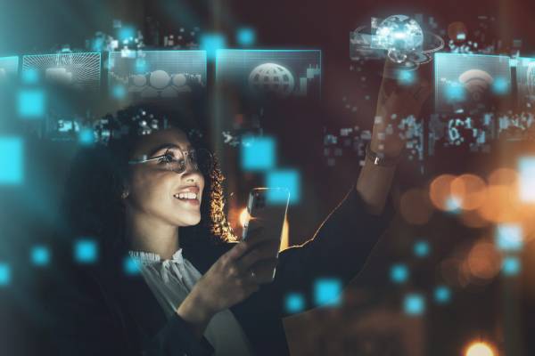 Image of a happy looking women working in the IT sector holding a mobile in one hand and touching the IT based virtual images displayed around her.