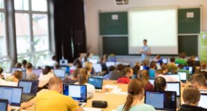 Rear view of students sitting and listening in a training room doing practical tasks on their laptops.